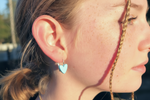 Close-up of a person wearing a blue heart-shaped earring.