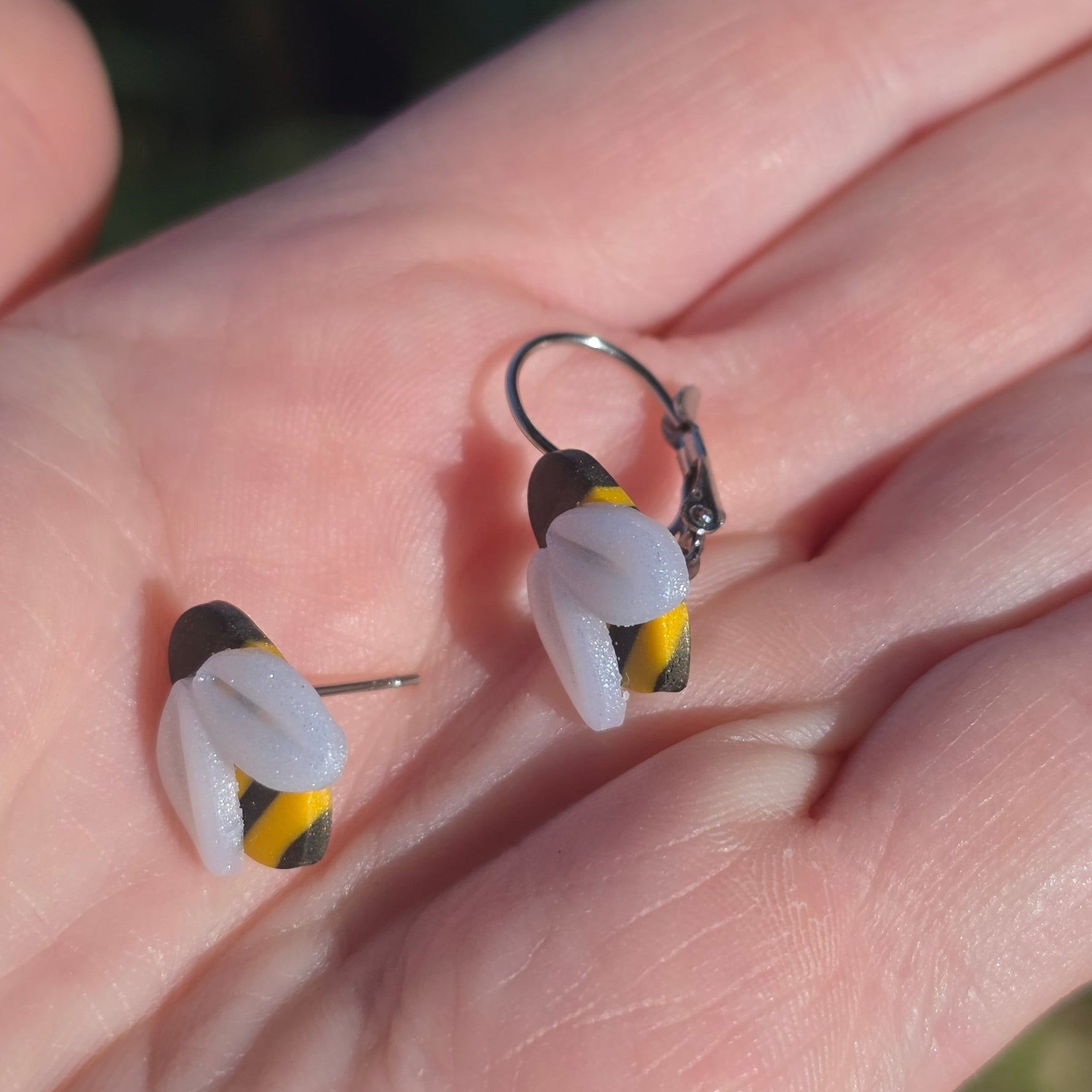 Oorsteker en bengelende bij oorbel uit zwart-geel gestreepte-polymeerklei met witte vleugeltjes, naast elkaar op een hand